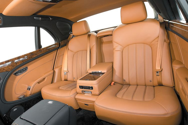 Сзади Mulsanne — словно кабинет: все строго и функционально. Наклон спинки дивана меняется только перемещением подушки вперед, что сокращает запас места для ног. Здесь тоже можно сесть втроем, но центральная консоль выпирает сильнее, чем в Роллс-Ройсе